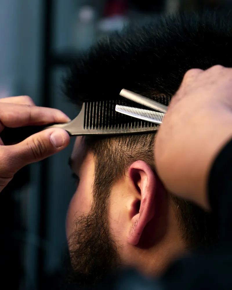 Barbero entresacando el pelo de un cliente con tijera y peine