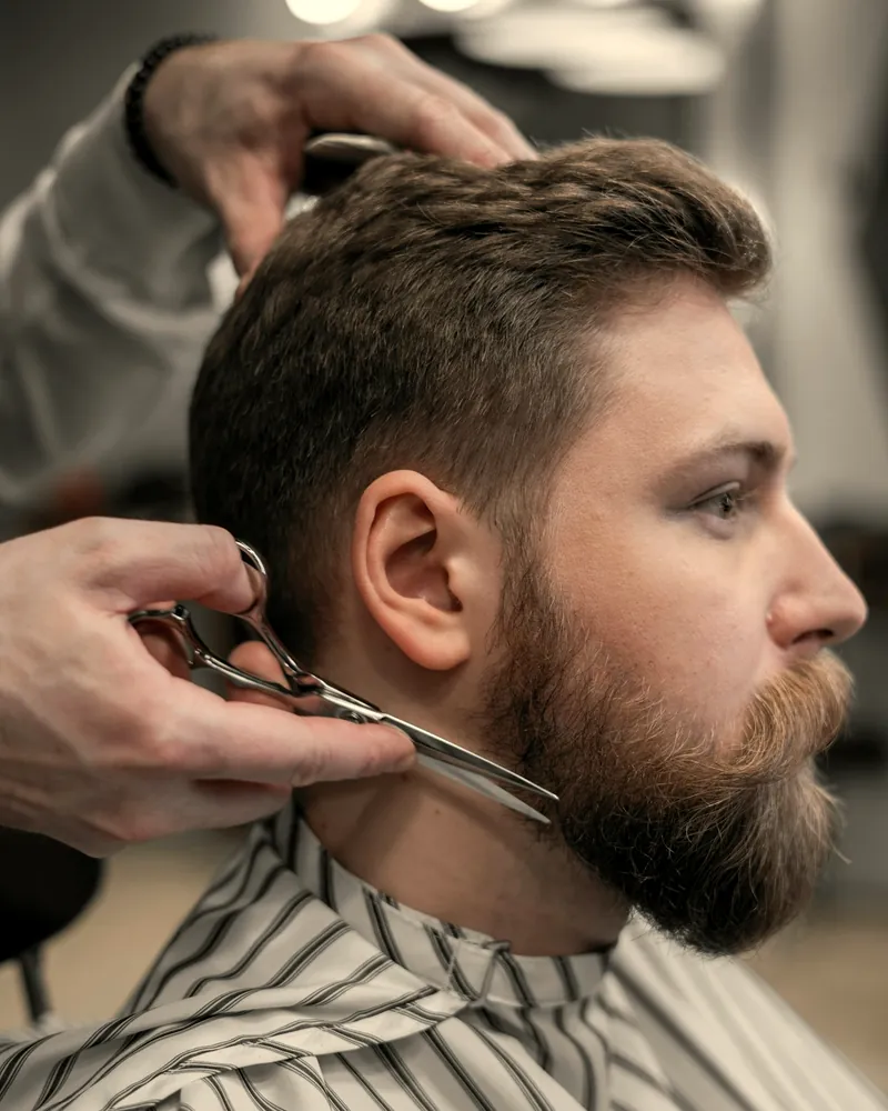 Barbero recortando con tijera la barba de un cliente